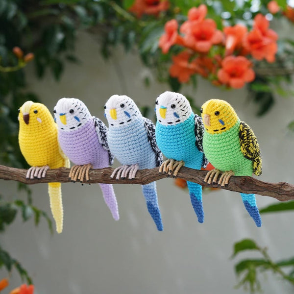Five colorful crochet parakeets on a branch with a floral background