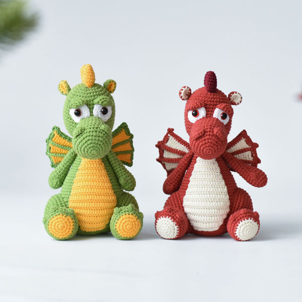 Two crocheted dragon toys, one green and yellow, the other red and white, on a light background.