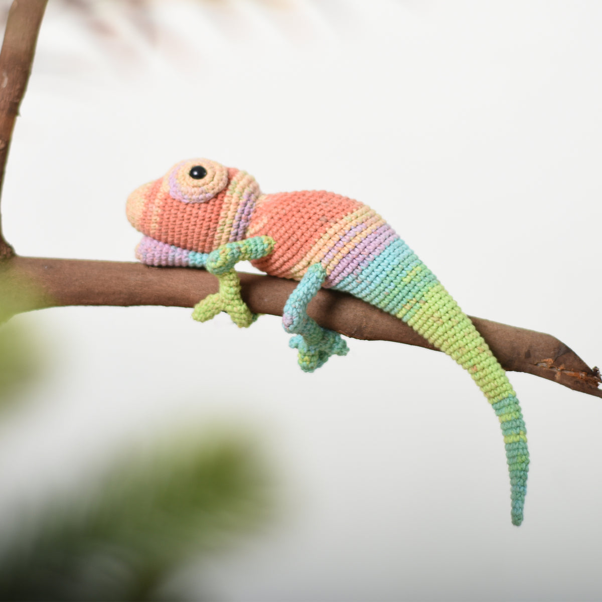 Multicolored crochet chameleon in coral, yellow, lavender, and green resting along a branch